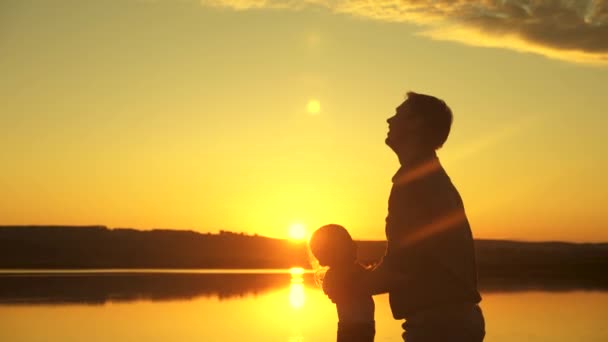 Papà getta la sua figlioletta felice in aria sulla spiaggia, divertendosi al tramonto. padre gioca con il bambino con l'acqua. felice concetto di famiglia. silhouette di un padre e un bambino sano che sorvola il sole — Video Stock