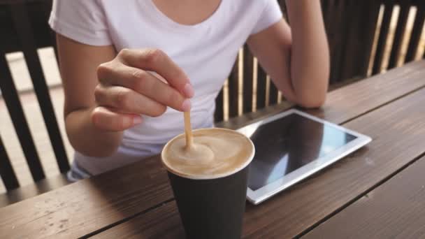 Une fille dans un café est en remuant délicieux café aromatique et en utilisant une tablette. femme bavarder boire du café et se reposer. — Video