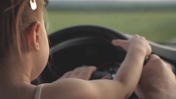 Dad teaches his little daughter to turn steering wheel while sitting in his car in drivers seat. father travels with children by car. driver and kid are driving. happy family and childhood concept — Stock Video