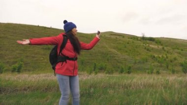 Sağlıklı ve neşeli bir kadın telefonla doğayı fotoğraflıyor. Özgür genç kız turist blogcu dağların eteklerinde arka planda güzel manzarası olan bir akıllı telefon kullanarak selfie videoları kaydediyor..