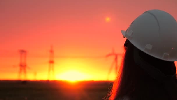 Una mujer ingeniera en un casco blanco inspecciona una línea eléctrica. Líneas eléctricas de alto voltaje al atardecer. Distribución y suministro de electricidad. energía limpia — Vídeos de Stock