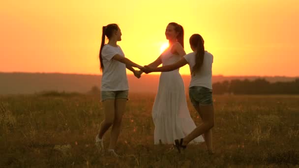 Mladá matka se zdravými dcerami a sestrami tančí společně v kruhu na slunci, baví se na poli, parku. Volná rodina si při západu slunce hraje na trávu. Šťastné rodinné dětství mateřství koncept — Stock video