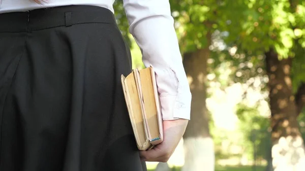 Chica adolescente se apresura a la escuela con libros. Una estudiante camina por la calle con libros de texto en sus manos en el parque de verano. colegiala en la ciudad. — Foto de Stock