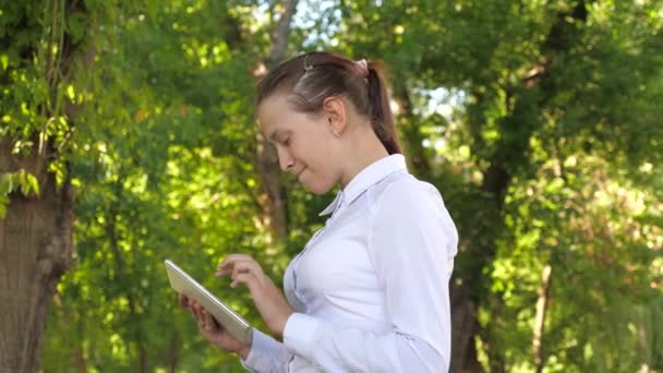 Női diák tanít az utcán egy táblagéppel a parkban. Egy fiatal lány portréja egy tablettel a kezében. Boldog nő olvasás jó hír egy külső üzenet. — Stock videók