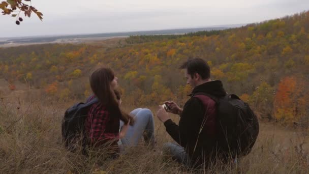 Reisende werden mit dem Smartphone vor der Kulisse einer wunderschönen Herbstlandschaft fotografiert. Freireisende Männer und Frauen mit Rucksäcken machen beim Entspannen ein Selfie. Teamwork der Reisenden. Reisekonzept — Stockvideo