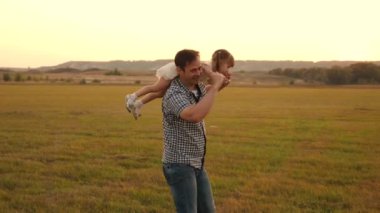 Baba gün batımında kızıyla birlikte omuzlarında yürüyor. Mutlu ve sağlıklı bir aile parkta dinleniyor. Babam güneşin altında sevgili çocuğunun omuzlarını taşıyor. Ebeveynleri olan çocuk gün batımında yürür.