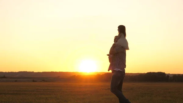 Papà porta sulle spalle del suo amato figlio sano al sole. Mio padre cammina con sua figlia sulle spalle nel parco. bambino con genitori cammina al tramonto. felice concetto di famiglia libera — Foto Stock