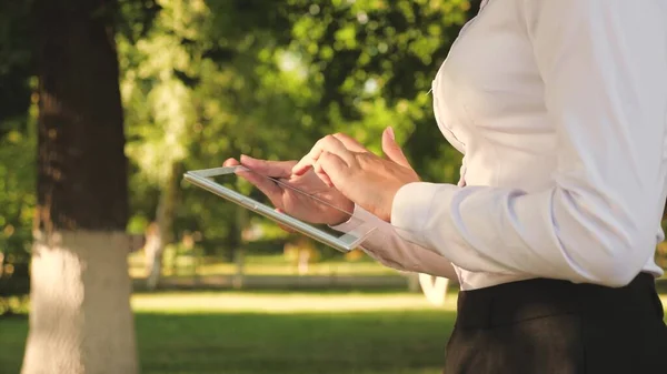 Portrait of a young girl with a tablet in her hand. female student teaches lessons on the street with a tablet in the park. Happy woman reading good news in an external message.