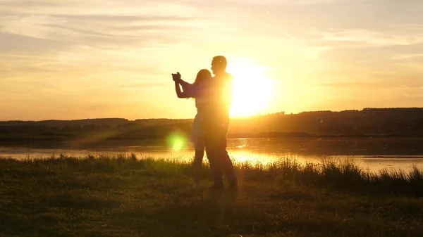 Joven pareja libre bailando al atardecer en la playa. Chico feliz y niña vals en la noche en un parque de verano. Enamorado hombre y mujer bailan en los brillantes rayos del sol en el fondo del lago. —  Fotos de Stock