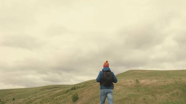 Um viajante feliz livre vai às montanhas de braços abertos, apanha vento com as mãos. jovem homem saudável viaja com uma mochila desfrutando de belas paisagens de montanhas e colinas. viagem e aventura — Fotografia de Stock