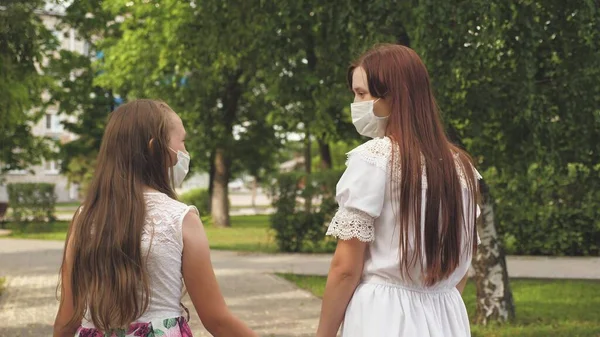 Tonåringar på gatan i staden reser i en medicinsk mask. två flickor i skyddsmasker går på sina ansikten utomhus i parken. skydda turister från virus. utomhus masker för att skydda mot infektion — Stockfoto