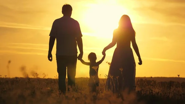 mom, dad and baby play outdoors. healthy little daughter jumps and flies in arms of mother and father in field at sunset. Happy family walks in the field in sun. concept of happy family of children.