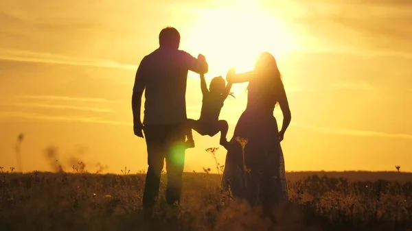 Mamma, pappa och barn leker utomhus. frisk liten dotter hoppar och flyger i armarna på mor och far i fält vid solnedgången. Glad familj går på fältet i solen. begreppet lycklig barnfamilj. — Stockfoto