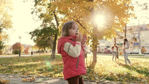 A little kid walks along path and smiles in sun. little child is playing in the autumn park with his family. daughters and mother walk together on day off. concept of a healthy family and childhood. — Stock Photo, Image