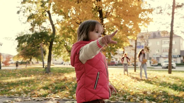 A little kid walks along path and smiles in sun. little child is playing in the autumn park with his family. daughters and mother walk together on day off. concept of a healthy family and childhood. — Stock Photo, Image
