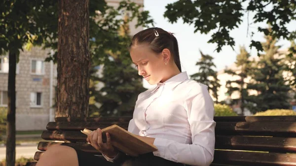 Schöne freie Frau, die gute Bücher liest. Studentin erteilt Unterricht auf der Straße mit einem Buch im Park auf einer Bank. Porträt eines jungen Mädchens mit einem Lehrbuch in der Hand. Junge Studentin bereitet sich auf Prüfungen vor — Stockfoto