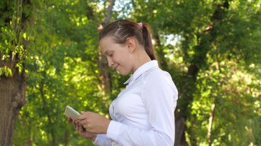 Bayan öğrenci parkta elinde tabletle sokakta ders veriyor. Elinde tabletle genç bir kızın portresi. Mutlu kadın dış mesajda iyi haberler okuyor..