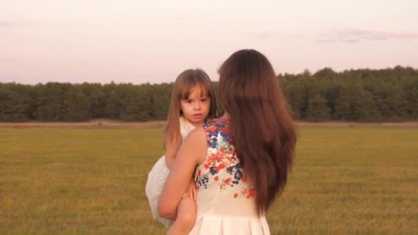 Mutlu anne, yaz yürüyüşünden sonra yorgun kızını kollarında taşır. Mutlu aile ve çocukluk kavramı. Anne ve kızı tarlada yürüyor.. — Stok video