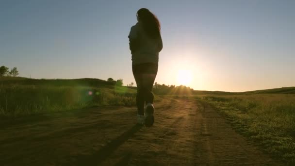 Gezond mooi meisje is bezig met fitness, joggen, silhouet. vrije jonge vrouw traint in de zomer in het park bij dageraad. Jogger girl ademt frisse lucht. 's Avonds lopen in prachtige zonnestralen. — Stockvideo