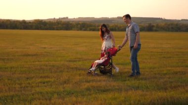 Doğada bebek arabasında küçük bir çocuğu olan sağlıklı bir aile. Mutlu özgür aile. Çocukluk kavramı. Sevgili küçük kızım güneşin arka planına karşı parkta bir bebek arabasına biniyor. Anne babanın sevgili çocuğu.