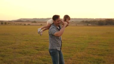 Baba gün batımında kızıyla birlikte omuzlarında yürüyor. Mutlu ve sağlıklı bir aile parkta dinleniyor. Babam güneşin altında sevgili çocuğunun omuzlarını taşıyor. Ebeveynleri olan çocuk gün batımında yürür.