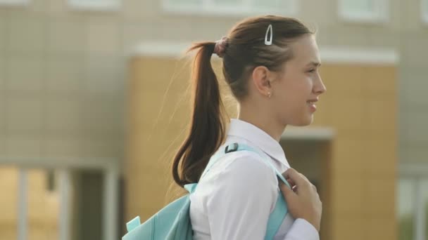 A school girl with a backpack goes down the street to school a beautiful young student goes to class. concept of education. a teenage girl hurries to class. — Stock Video