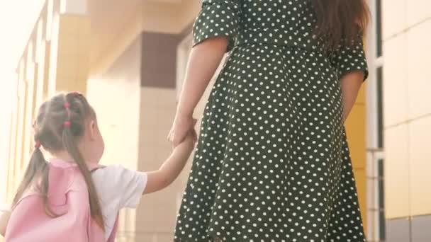 Lilla dotter skolflicka går med en ryggsäck och håller sin mammas hand. Förskoleutbildningskoncept. lycklig familj mor och barn gå till skolan hålla hand. — Stockvideo