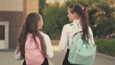 Sırt çantalı liseli kızlar sokakta okula giderler. Kız arkadaşlar okula gider. Onlar çok eğleniyorlar. Eğitim konsepti. Sağlıklı gençler açık hava derslerine giderler. Kızlar okul bahçesinde sohbet eder ve konuşur.