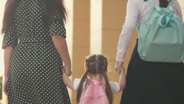 Glada barnhoppning. Lycklig familj mor och barn går i skolan hålla hand. lilla dotter skolflicka går med en ryggsäck och håller hand mor och syster. skolutbildningskoncept. — Stockvideo