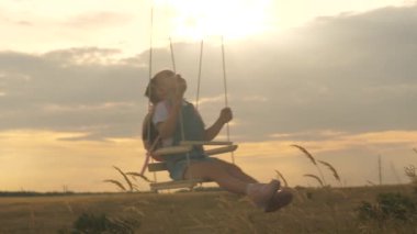 Sağlıklı, mutlu bir çocuk parkta salıncakta sallanıyor. Küçük neşeli kız uçarken gülüyor, seviniyor ve kollarını sallıyor. Annem kızını güneşin altında salıncakta sallıyor. Çocukluk ve