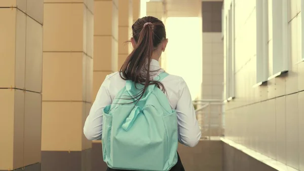 Una colegiala con una mochila va calle abajo a la escuela un joven estudiante hermoso va a clase. concepto de educación. una adolescente se apresura a clase. — Foto de Stock