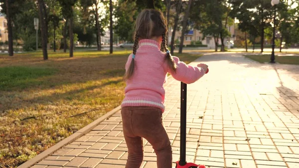 Lilla flickan lär sig cykla. En lycklig liten flicka som leker i parken. hälsosam unge rider en skoter i staden på gatan. Glad barndom — Stockfoto