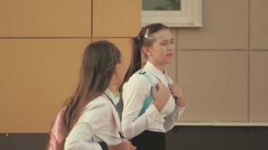 Sırt çantalı liseli kızlar sokakta okula giderler. Kız arkadaşlar okula gider. Onlar çok eğleniyorlar. Eğitim konsepti. Sağlıklı gençler açık hava derslerine giderler. Kızlar okul bahçesinde sohbet eder ve konuşur.