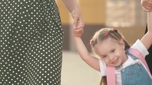 En frisk liten dotter leker med sin mor och syster, håller sina händer och hoppar. familje- och barndomskoncept. Glada barnhoppning. lycklig familj, mor och barn går till skolan innehav — Stockvideo