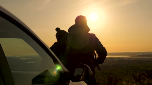 Šťastní cestovatelé muž a žena stojí vedle auta a obdivovat krásný západ slunce z kopce. turisté cestují autem a obdivují východ slunce, les a řeku. Volní cestující, turisté. — Stock video