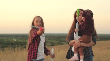 Mutlu anne ve çocuklar birlikte oynar, üfler ve sabun köpükleri yakalar. Kız kardeşler gün batımında parkta birlikte oynarlar. Mutlu aile ve çocukluk kavramı. Güneşin altında kabarcıklar, çocukların doğum günü