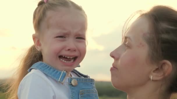 Madre joven abraza y calma a su hija pequeña, el bebé está llorando en el parque en brazos de mamá. familia madre e hijo con lágrimas en los ojos abraza a su madre, emocionalmente. Mamá calma al bebé.. — Vídeo de stock