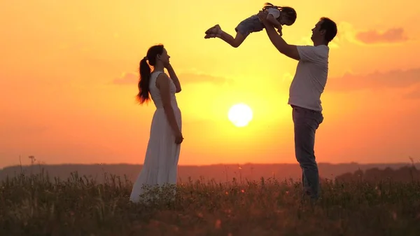 Papà gioca con la sua figlioletta, felice di lanciare il bambino in aria, mamma felice ammira la sua famiglia. Mamma, papa 'e bambino, la famiglia sta riposando al tramonto sul campo. felice famiglia sana camminando all'aria aperta. — Foto Stock