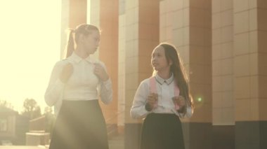 Kız arkadaşlar okula gider. Onlar çok eğleniyorlar. Sırt çantalı okul kızları sokakta okula gider. Eğitim konsepti. Sağlıklı gençler açık hava derslerine giderler. Kızlar okul bahçesinde sohbet eder ve konuşur.