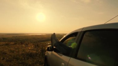 Genç bir kadın arabayla seyahat etmeyi, bacaklarını açık pencereden dışarı uzatmayı ve güneşin doğuşunu seyretmeyi sever. Bedava gezginler, turistler. Özgür kız arabada dinleniyor ve dağdan gelen güzel günbatımına hayran..