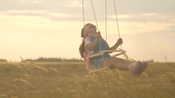Malá veselá holčička se zasměje, raduje se z letu na houpačce. zdravé šťastné dítě jezdí na laně houpačka na větvi v parku. Máma s tátou si hrají se svou dcerou na houpačce pod stromem na slunci. šťastná rodina — Stock video