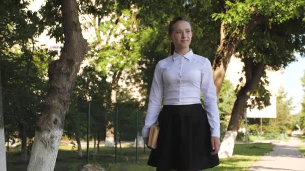 Beautiful student walks down the street with textbooks in a summer park. schoolgirl in the city. teen girl hurrying to school with books — Stock Video