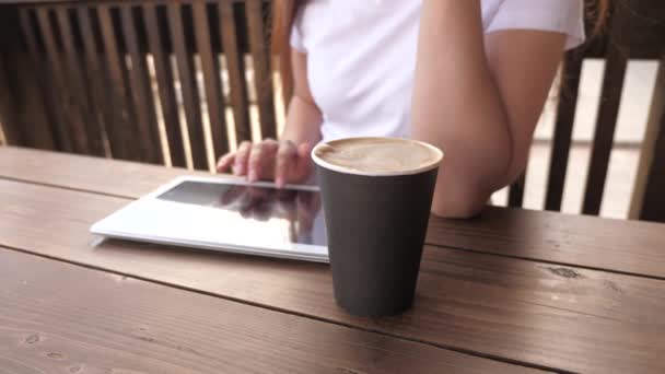 Eine junge Frau im Café arbeitet mit einem Gadget. Nahaufnahme. Ein Mädchen in einem Sommercafé nimmt ein Tablet und trinkt köstlichen aromatischen Kaffee. Frau plaudert, trinkt Kaffee und entspannt. — Stockvideo