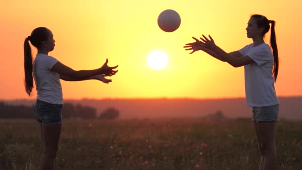 Dospívající dívky házet míč na sebe v teplém slunci. šťastné zdravé děti, které si při západu slunce hrají s míčem na zelené louce. šťastný rodinný a dětský koncept. Veselá rodina si užívá letní venkovní zábavu — Stock video