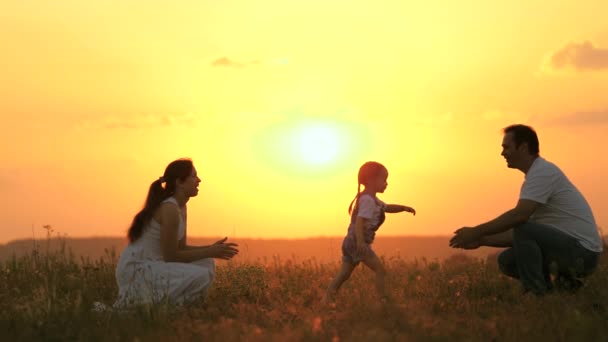 Figlioletta va da mamma a papà, abbraccia e bacia i suoi genitori in raggi di un sole caldo. Felice famiglia passeggiate nel parco al tramonto. Mamma, papa 'e bambino. famiglia sana gioca sul campo. Concetto famiglia felice — Video Stock