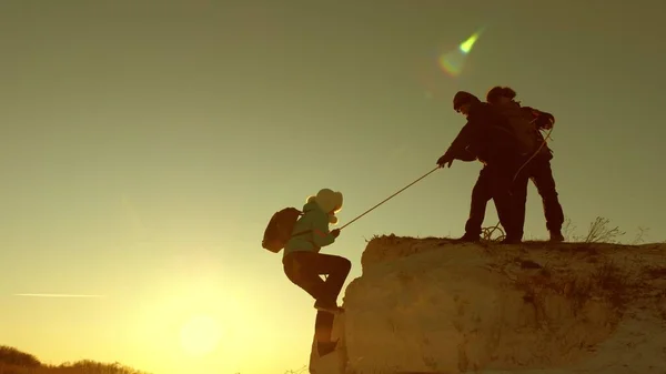 Climbers climb mountain on a rope. a male tourist helps a girl traveler to climb mountain. Travel and adventure in mountains at sunset. teamwork of tourists in sun. freedom and adventure concept — Stock Photo, Image