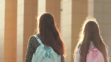 Anne ve kız öğrenci bir sırt çantasıyla gidip annelerinin elini tutuyor. Okul eğitimi konsepti. Mutlu aile annesi ve çocuğu el ele tutuşarak okula gider..