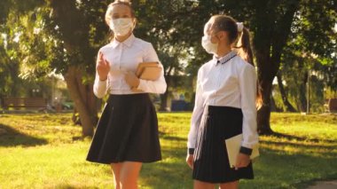 Okullu kızlar sokakta maske takarak, ders kitabı ve tablet tutarak yürüyorlar. Gençler parktan geçip okula giderler. Kızlar tıbbi maskelerle dolaşır. Virüs ve bakterilerden korunurlar..