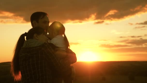 Glada familjekramar i solen. Pappa kramar mamma och dotter på kvällen i parken vid solnedgången. hälsosam baby i famnen på pappa. Glada barn, mor och far leker. lycklig familj och barndom — Stockvideo