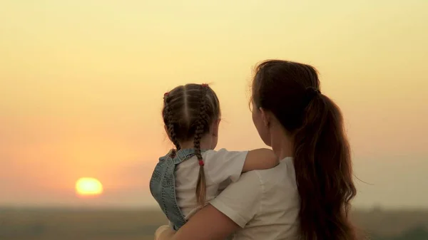 Mamma leker med sin dotter och visar barnet solnedgången. Lycklig familj, mamma och dotter på fältet tittar på solen. Begreppet lycklig familj och friska barn. Barnet älskar mamma. — Stockfoto